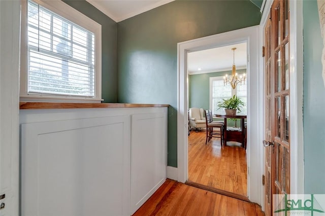 laundry area with a chandelier, plenty of natural light, crown molding, and light wood-type flooring