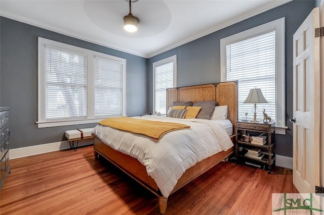 bedroom with crown molding, multiple windows, light wood-style floors, and baseboards