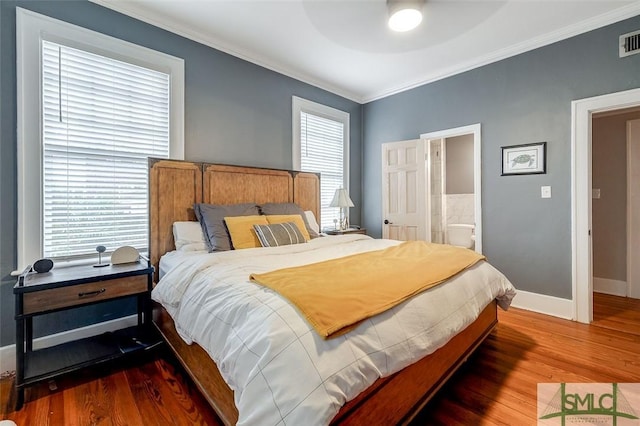 bedroom featuring visible vents, ensuite bath, wood finished floors, crown molding, and baseboards