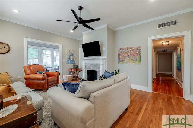 living area featuring a ceiling fan, visible vents, a premium fireplace, light wood-style flooring, and ornamental molding