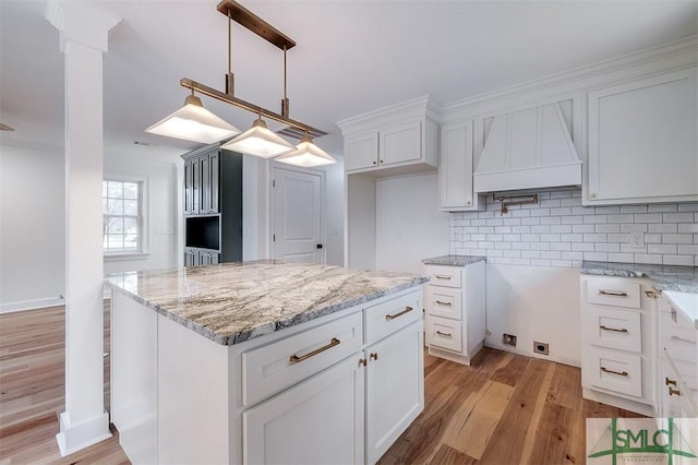 kitchen with tasteful backsplash, light stone countertops, pendant lighting, light wood-style floors, and white cabinets