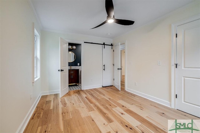 unfurnished bedroom with baseboards, ornamental molding, light wood-style floors, a barn door, and connected bathroom