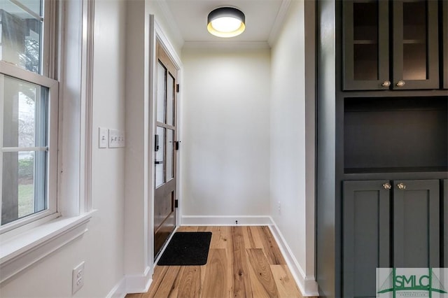 doorway to outside with baseboards, crown molding, and light wood-style floors