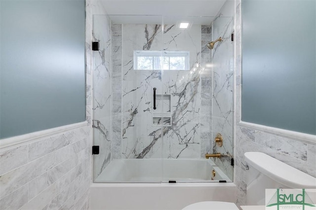 full bathroom with tile walls, toilet, a wainscoted wall, and shower / bath combination with glass door