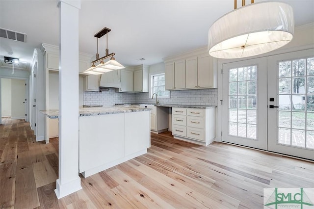 kitchen featuring light stone counters, visible vents, light wood-style flooring, ornamental molding, and backsplash