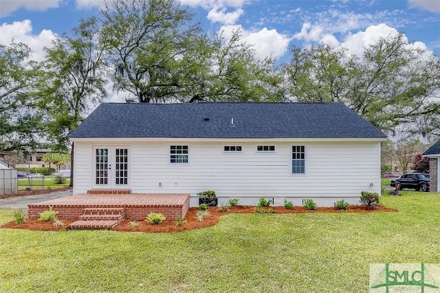 rear view of property with french doors, a lawn, and roof with shingles