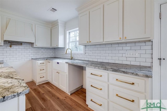 kitchen with premium range hood, visible vents, light stone counters, and decorative backsplash