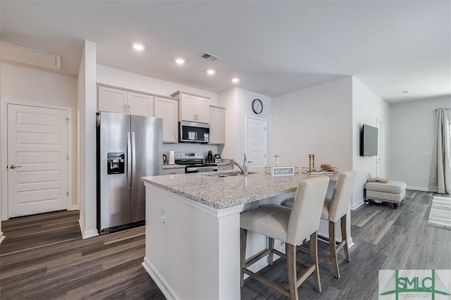 kitchen featuring visible vents, dark wood finished floors, a sink, appliances with stainless steel finishes, and a kitchen bar