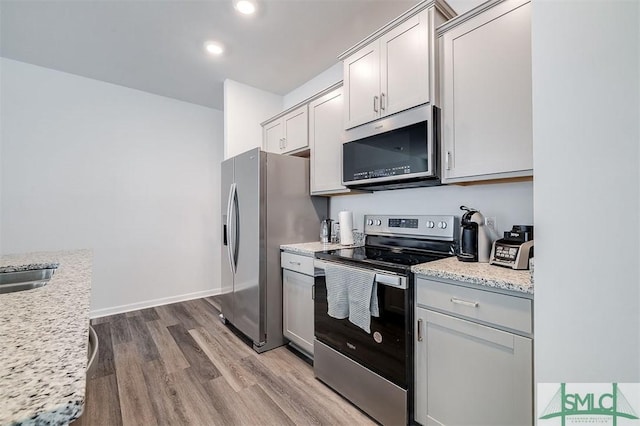 kitchen featuring wood finished floors, recessed lighting, appliances with stainless steel finishes, baseboards, and light stone countertops