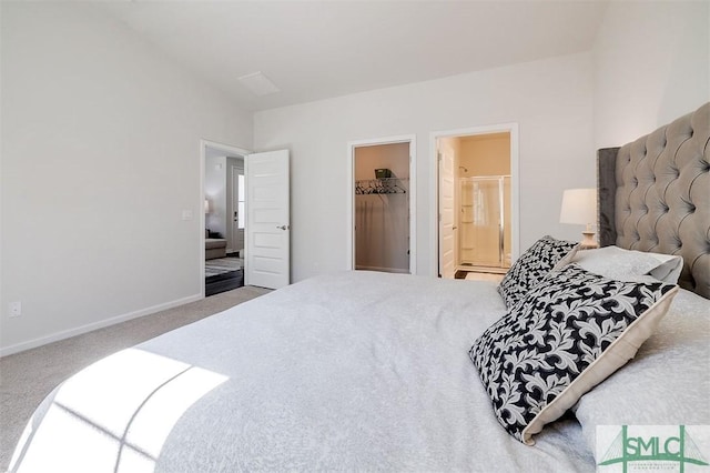 carpeted bedroom featuring ensuite bathroom, a walk in closet, baseboards, and vaulted ceiling