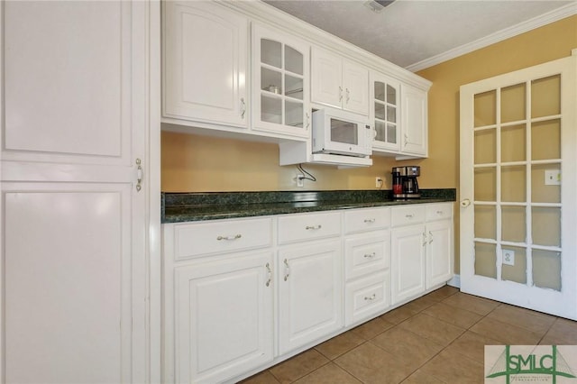 kitchen with white microwave, glass insert cabinets, ornamental molding, tile patterned floors, and white cabinetry