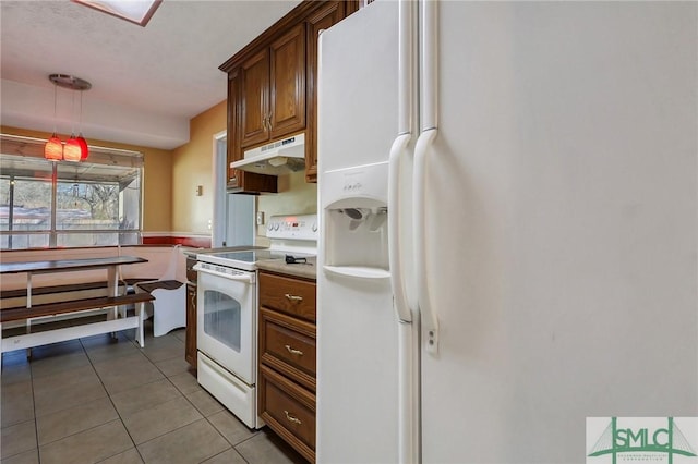 kitchen with under cabinet range hood, decorative light fixtures, light tile patterned floors, brown cabinetry, and white appliances