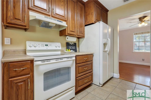 kitchen featuring under cabinet range hood, light tile patterned floors, brown cabinets, white appliances, and a ceiling fan