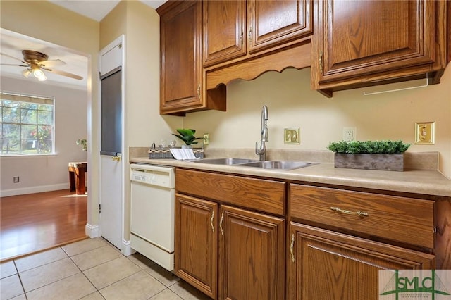 kitchen with light tile patterned floors, white dishwasher, a sink, light countertops, and brown cabinets