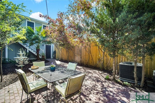 view of patio with outdoor dining area, fence, central AC, and a hot tub