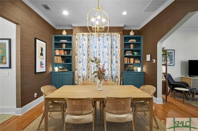 dining area featuring arched walkways, an inviting chandelier, light wood-style flooring, and crown molding