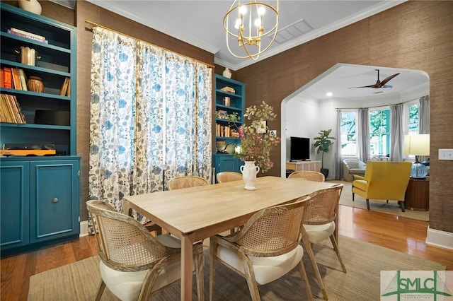 dining space featuring wood finished floors, arched walkways, ornamental molding, and ceiling fan with notable chandelier