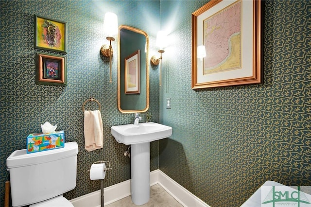 half bathroom with wallpapered walls, toilet, baseboards, and a sink