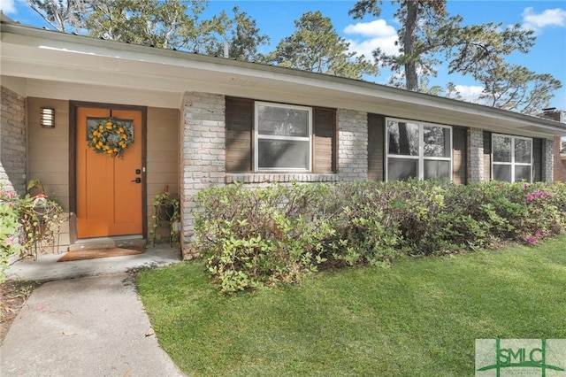 view of exterior entry featuring brick siding and a yard