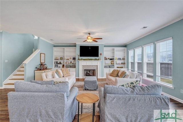 living area featuring wood finished floors, stairway, a fireplace, crown molding, and baseboards