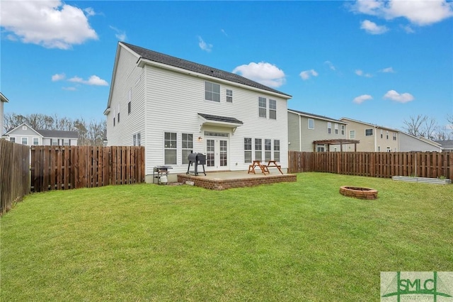 rear view of property featuring a fire pit, a lawn, a fenced backyard, and a patio area