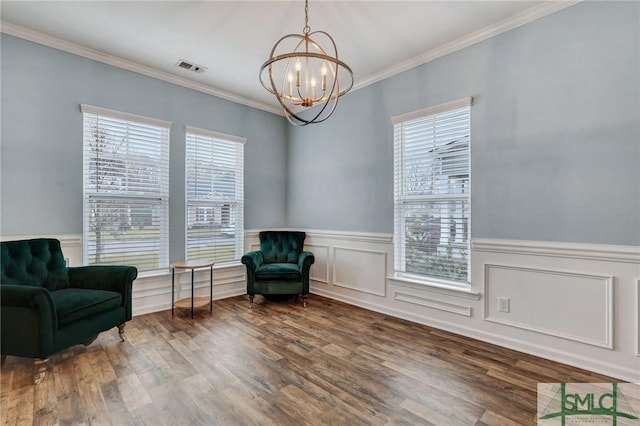 living area with visible vents, ornamental molding, wainscoting, wood finished floors, and a notable chandelier