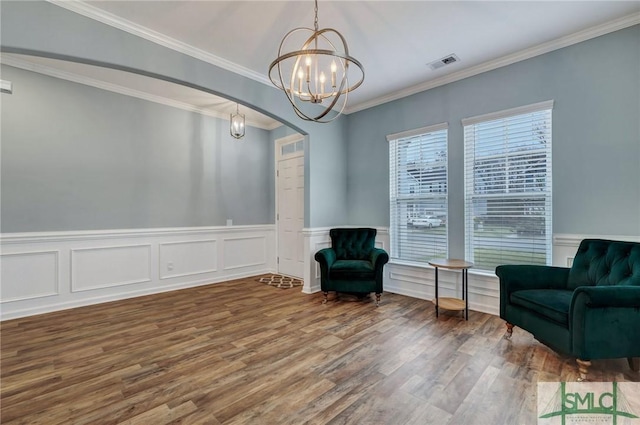 living area featuring wood finished floors, visible vents, an inviting chandelier, arched walkways, and crown molding