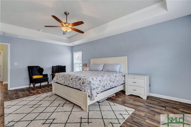 bedroom featuring a tray ceiling, wood finished floors, baseboards, and visible vents