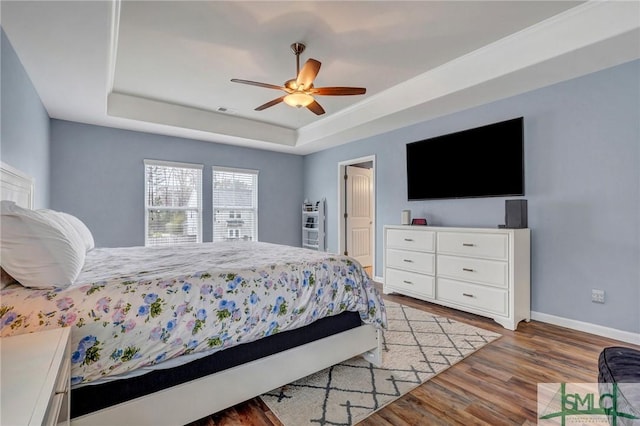 bedroom with visible vents, a tray ceiling, light wood finished floors, baseboards, and ceiling fan