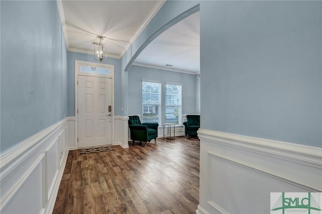 foyer entrance with wood finished floors, a wainscoted wall, arched walkways, and ornamental molding