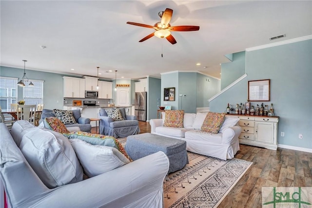 living room with visible vents, ceiling fan, baseboards, ornamental molding, and wood finished floors