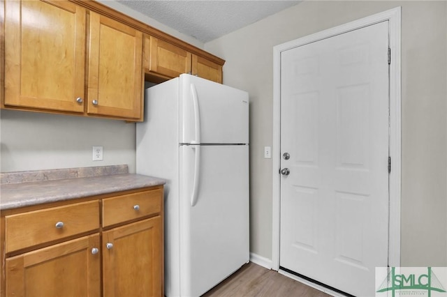 kitchen featuring light countertops, brown cabinets, freestanding refrigerator, light wood-style floors, and a textured ceiling