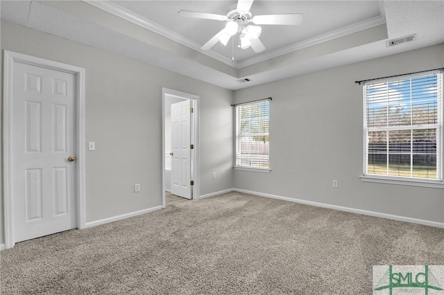 unfurnished bedroom featuring a tray ceiling, carpet, visible vents, and ornamental molding