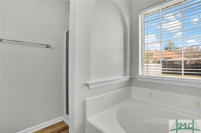 full bathroom with a bath, wood finished floors, and baseboards