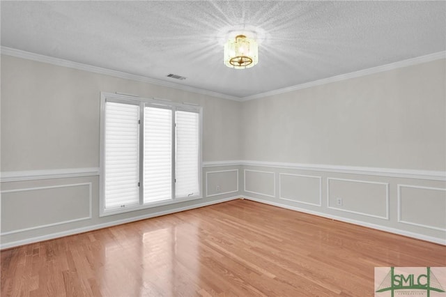 empty room with a textured ceiling, wood finished floors, and ornamental molding