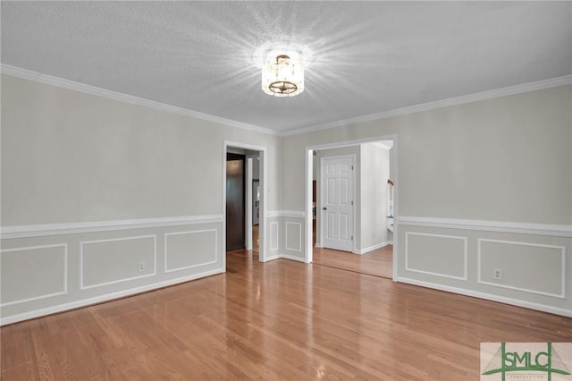 empty room with a decorative wall, a textured ceiling, crown molding, and wood finished floors