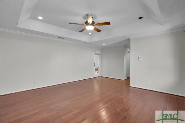 empty room with a raised ceiling, a ceiling fan, wood finished floors, crown molding, and baseboards