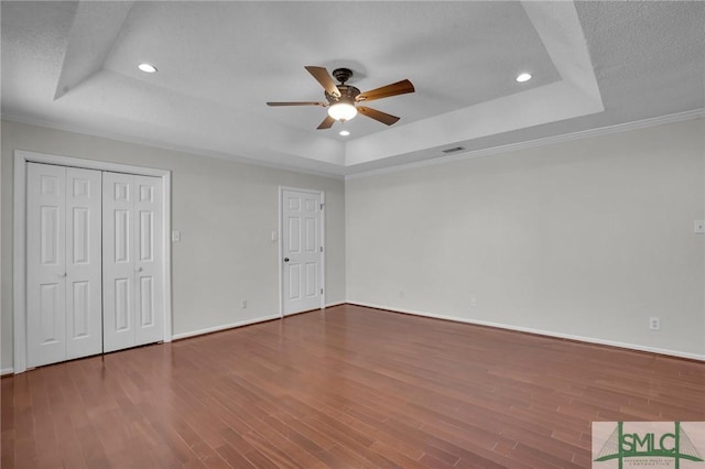 unfurnished bedroom with a raised ceiling, recessed lighting, wood finished floors, and baseboards