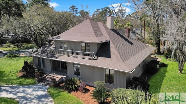 exterior space featuring a chimney, a front lawn, a balcony, and a shingled roof