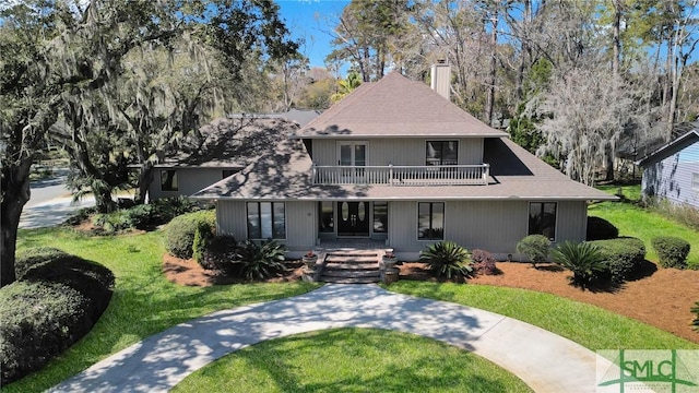 view of front of home featuring a front lawn, a porch, roof with shingles, a balcony, and a chimney