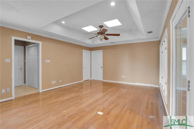 unfurnished room with baseboards, visible vents, light wood finished floors, a tray ceiling, and a skylight