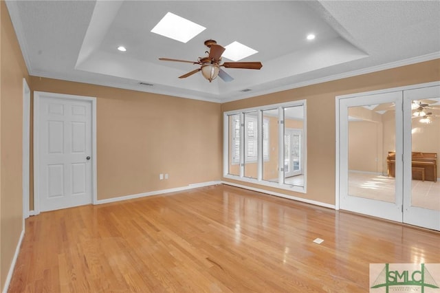 spare room with light wood-type flooring, a skylight, a raised ceiling, and ceiling fan