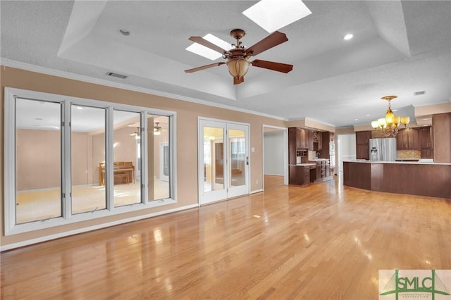 unfurnished living room with visible vents, light wood-type flooring, ornamental molding, a skylight, and a raised ceiling