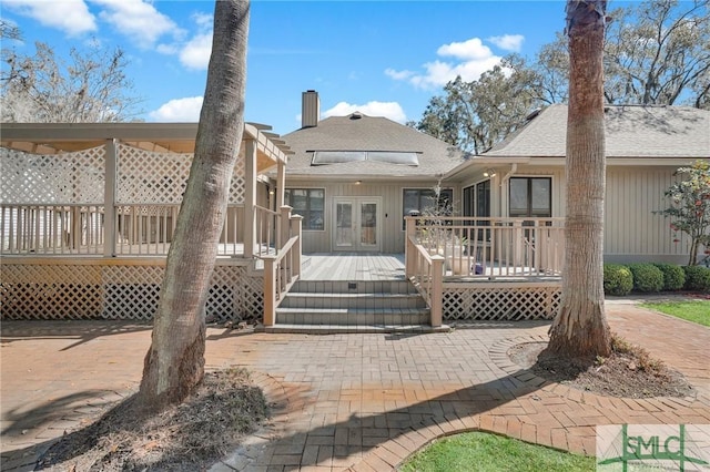 back of house with a wooden deck, french doors, a shingled roof, and a chimney