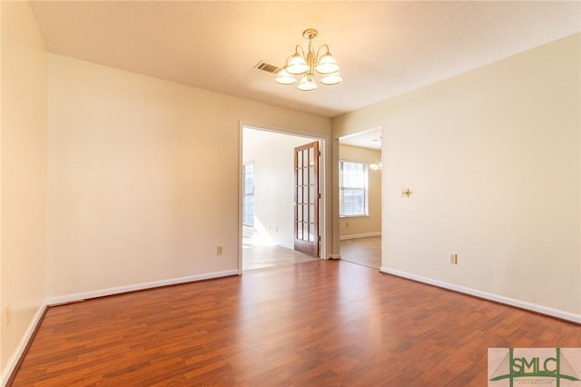 unfurnished room with a notable chandelier, wood finished floors, visible vents, and baseboards