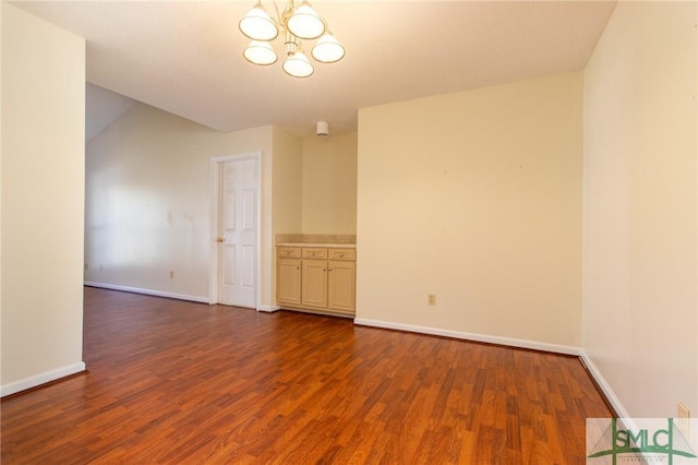 unfurnished room with dark wood finished floors, a notable chandelier, and baseboards