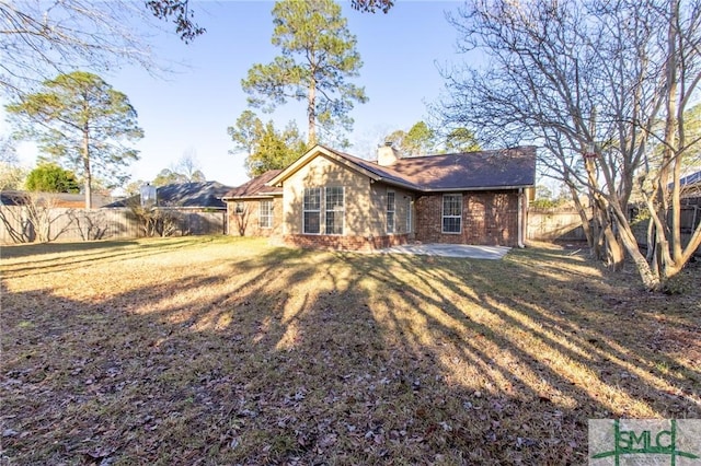 rear view of property featuring a patio, a yard, a fenced backyard, a chimney, and brick siding