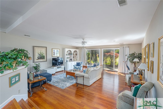 living room featuring a ceiling fan, built in shelves, wood finished floors, and visible vents