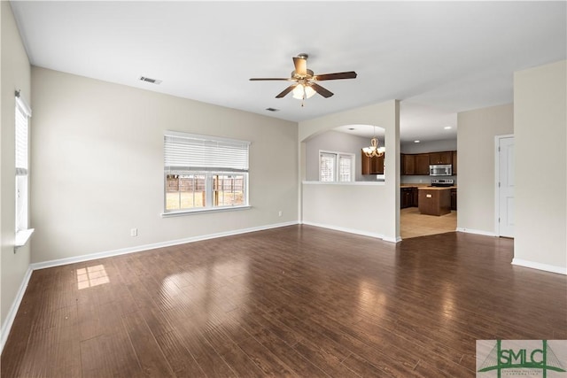 unfurnished living room featuring ceiling fan with notable chandelier, wood finished floors, recessed lighting, arched walkways, and baseboards