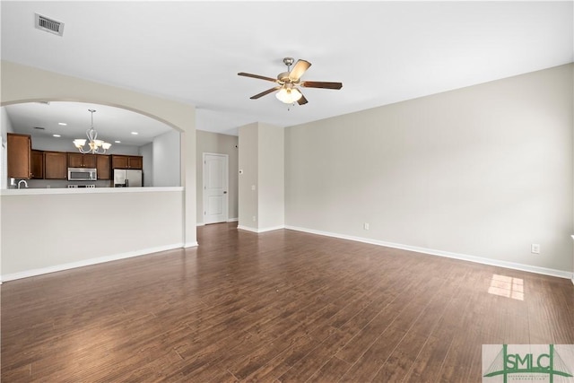 unfurnished living room featuring visible vents, baseboards, ceiling fan with notable chandelier, arched walkways, and dark wood-style floors